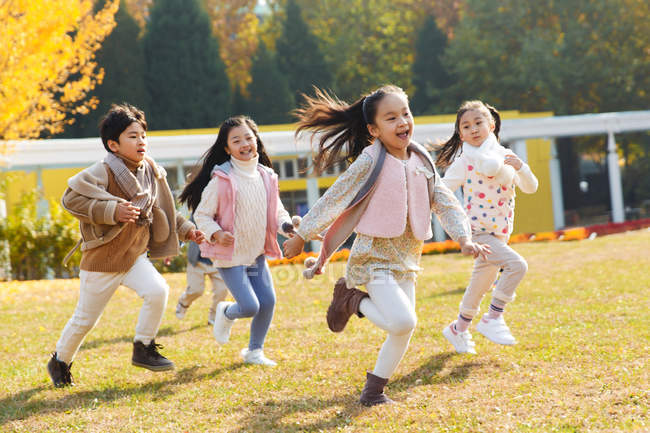 Счастливые мальчики и девочки, играющие вместе и бегающие на каруселях в парке — стоковое фото