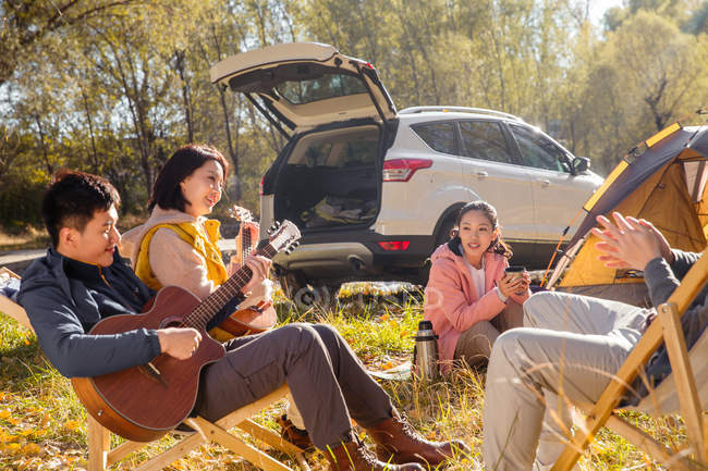 Man playing guitar for asian friends in autumnal forest — Stock Photo
