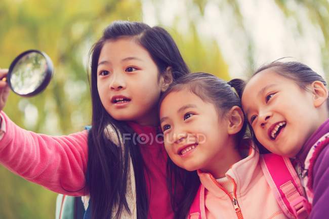 Три чарівні азіатські діти обіймаються і дивляться на збільшення скла в автономному парку — стокове фото