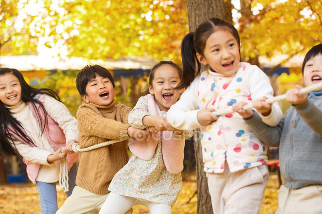 Fünf entzückende glückliche asiatische Kinder, die im herbstlichen Park gemeinsam Seil ziehen — Stockfoto