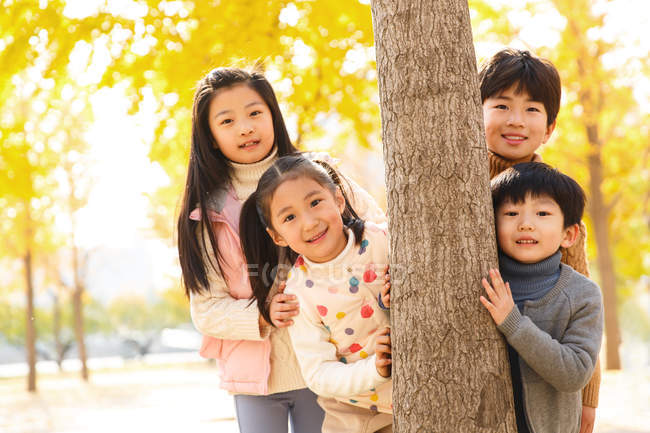 Meninos e meninas felizes de pé juntos perto da árvore e sorrindo para a câmera no parque de outono — Fotografia de Stock