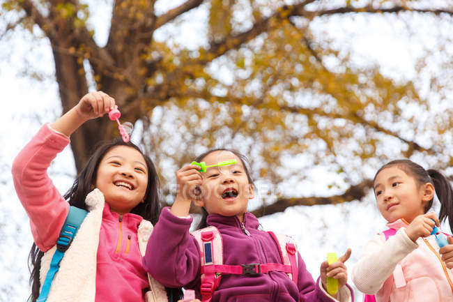 Baixo ângulo vista de três adorável asiático crianças soprando sabão bolhas no outonal parque — Fotografia de Stock