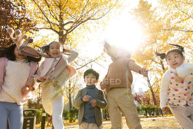 Низкий угол обзора пяти восхитительных счастливых детей, бегущих в осеннем парке — стоковое фото