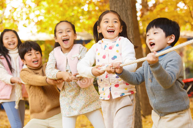 Cinq adorable heureux asiatique enfants tirant corde ensemble dans automnal parc — Photo de stock