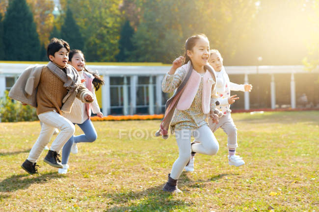 Happy boy and girls playing together and running on meadow in park — Stock Photo