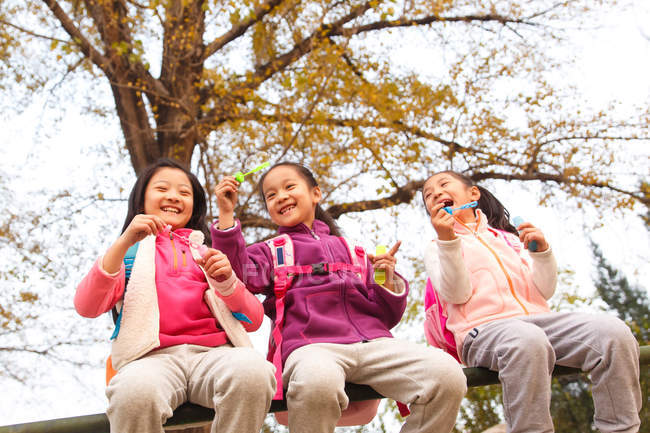 Low angle view of three adorable asian kids blowing soap bubbles in autumnal park — Stock Photo
