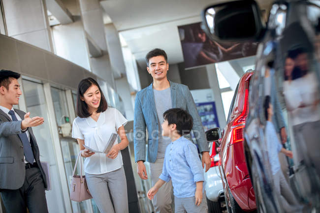 Venditore asiatico mostrando auto per felice famiglia scelta veicolo a car showroom — Foto stock