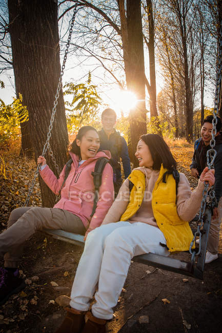 Hommes asiatiques poussant les femmes heureuses sur swing dans la forêt automnale — Photo de stock