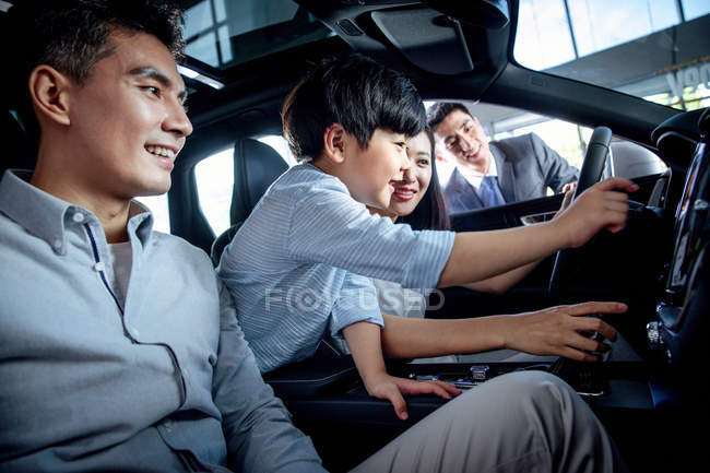 Família asiática com garoto testando carro no showroom — Fotografia de Stock