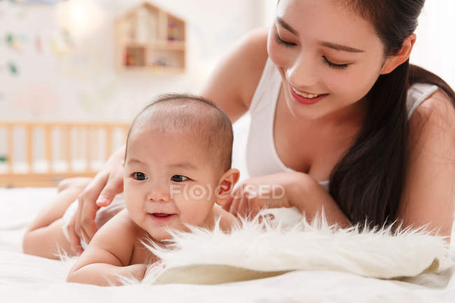 Glückliche junge Mutter blickt auf entzückendes Baby, das im Bett liegt — Stockfoto