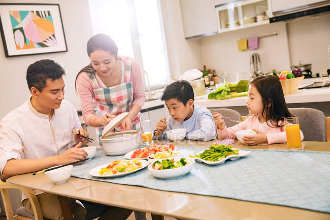 Счастливая китайская семья с двумя детьми, которые едят вместе дома — стоковое фото