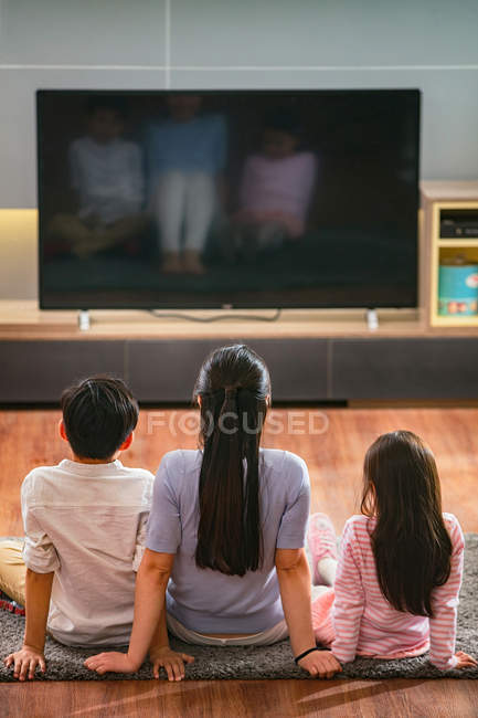 Vue grand angle de la mère avec deux enfants assis sur le tapis et regarder la télévision avec écran blanc — Photo de stock