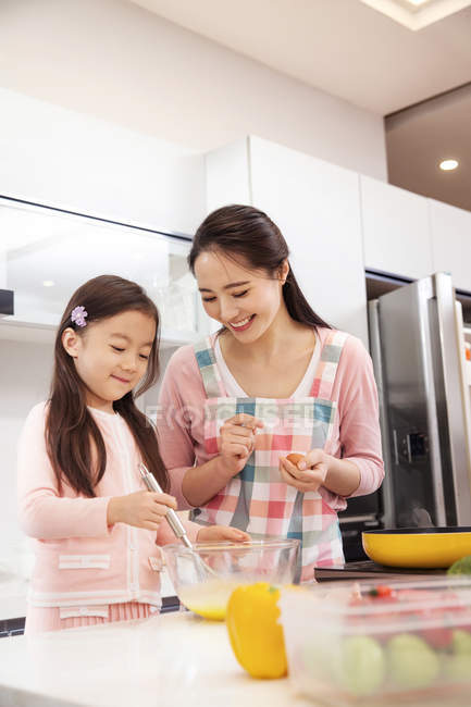 Feliz jovem asiático mãe e filha batendo ovos juntos na cozinha — Fotografia de Stock