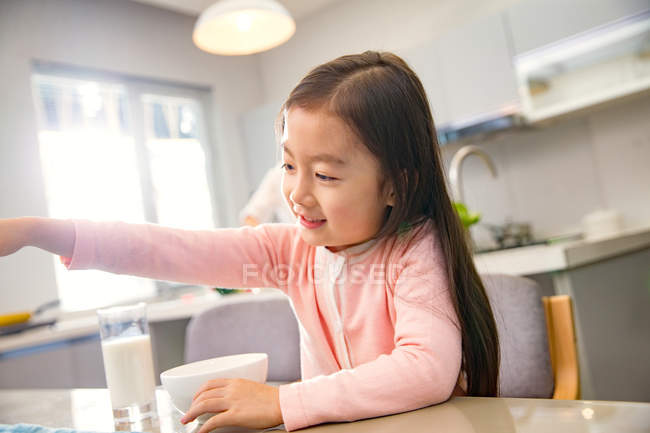 Entzückend glückliches chinesisches Kind sitzt beim Frühstück am Tisch — Stockfoto