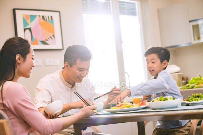 Счастливая азиатская семья с одним ребенком, сидящим за столом и едят вместе — стоковое фото