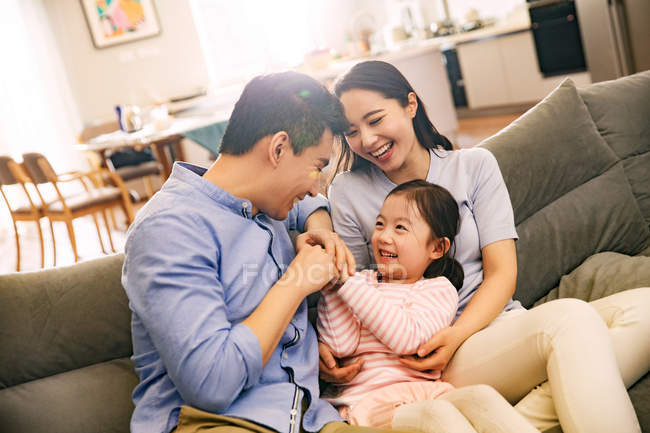 Счастливые родители с очаровательной маленькой дочерью веселятся вместе на диване — стоковое фото