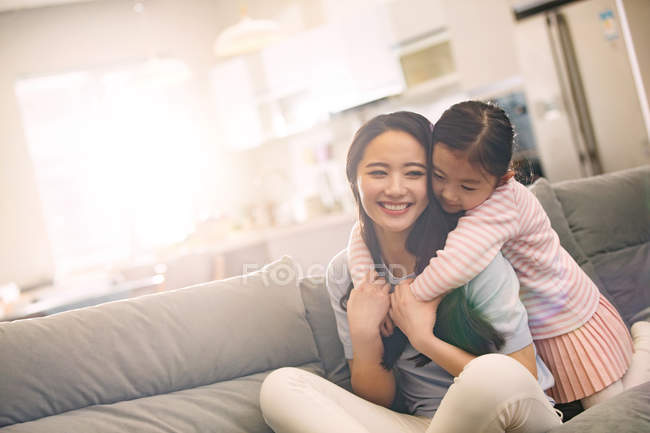 Heureux jeune asiatique mère avec adorable petite fille câlin ensemble sur canapé — Photo de stock