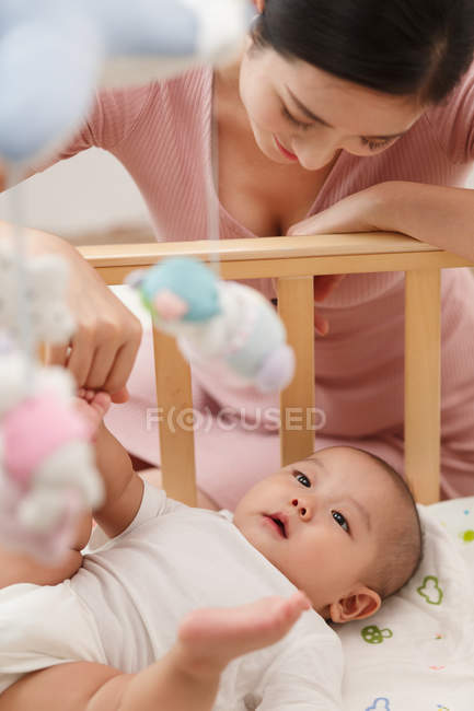 Щаслива молода мати дивиться на чарівну дитину, що лежить в ліжечку — стокове фото