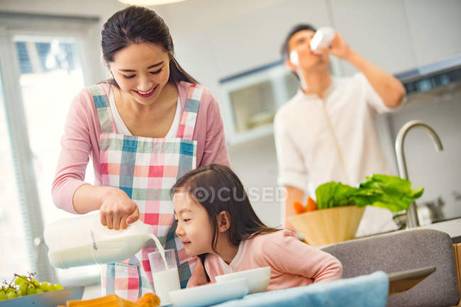 Smiling young mother pouring milk to adorable little daughter in kitchen — Stock Photo
