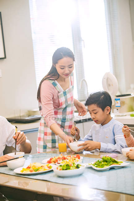 Tiro recortado de família chinesa feliz com duas crianças comendo juntos em casa — Fotografia de Stock