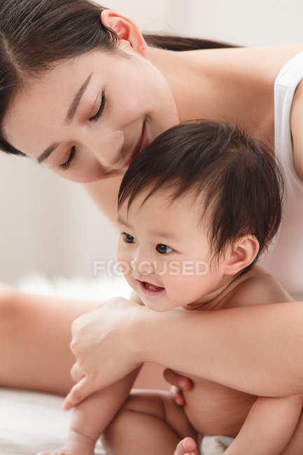 Feliz joven madre abrazando adorable sonriente bebé en pañal - foto de stock