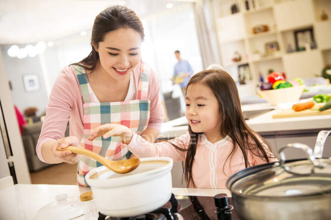 Красива щаслива молода мати з чарівною маленькою дочкою, що готує разом на кухні — стокове фото