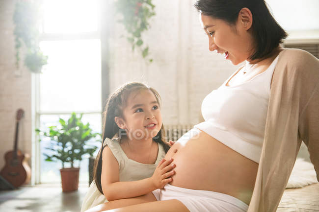 Прелестный маленький ребенок трогает живот беременной матери дома — стоковое фото