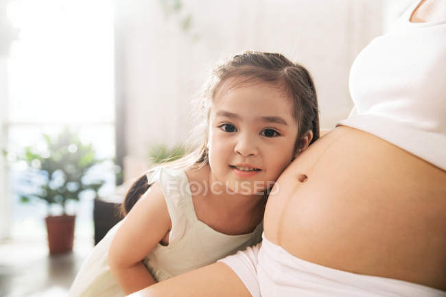Tiro cortado de menina feliz ouvindo barriga de mãe grávida — Fotografia de Stock