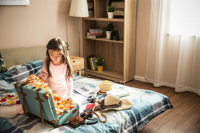 Alto angolo vista di adorabile poco asiatico ragazza imballaggio valigia su letto — Foto stock