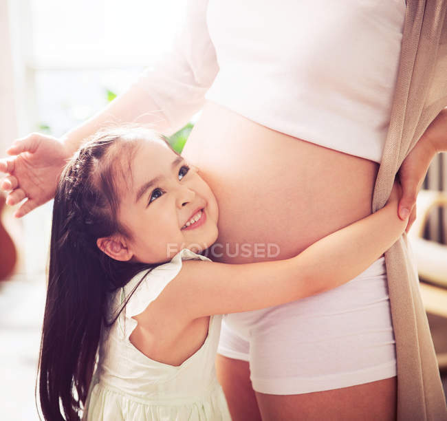 Adorable feliz niña abrazando embarazada madre, tiro recortado - foto de stock