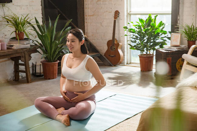 Sorrindo jovem grávida em sportswear sentado em tapetes de ioga em casa — Fotografia de Stock