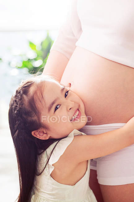 Гарненька щаслива дівчинка, яка обіймає вагітну матір вдома, підстрелена. — стокове фото