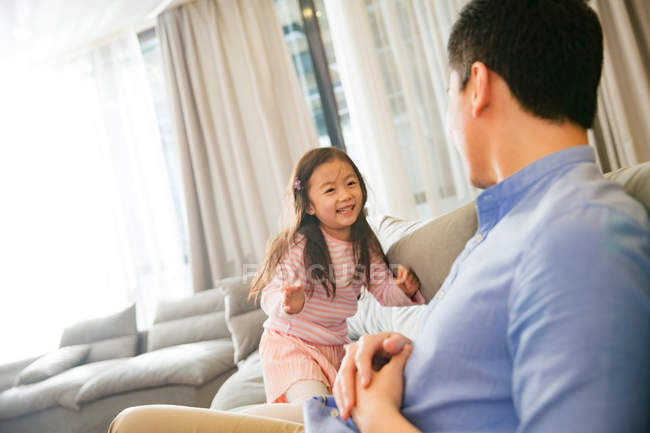 Счастливый китайский отец и очаровательная маленькая дочь играют и веселятся вместе на диване — стоковое фото