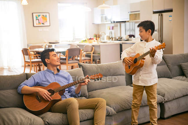 Felice padre asiatico e figlio giocando chitarre e sorridendo a casa — Foto stock