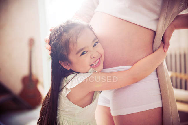 Cropped shot of cute happy little daughter hugging pregnant mother at home — Stock Photo