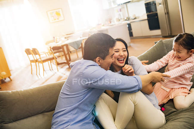 Щасливі батьки з чарівною маленькою дочкою розважаються разом на дивані — стокове фото
