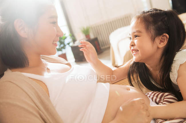 Adorable little child touching belly and playing with pregnant mother at home — Stock Photo