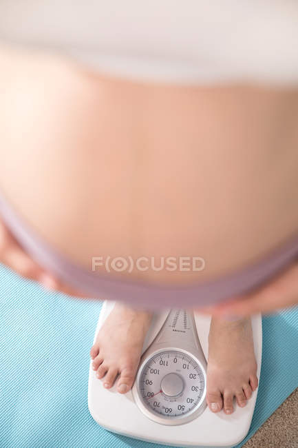 Обрізаний знімок молодої вагітної жінки, що стоїть на масштабах, селективний фокус — стокове фото