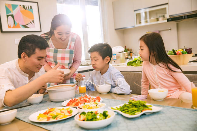 Familia china feliz con dos niños comiendo juntos en casa - foto de stock