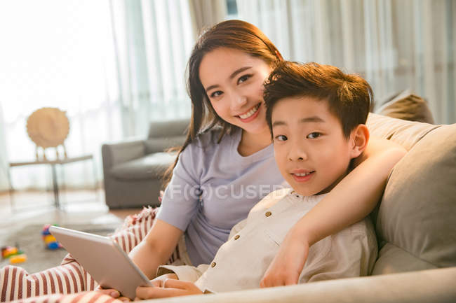 Mère heureuse avec son fils en utilisant une tablette numérique et souriant à la caméra ensemble à la maison — Photo de stock