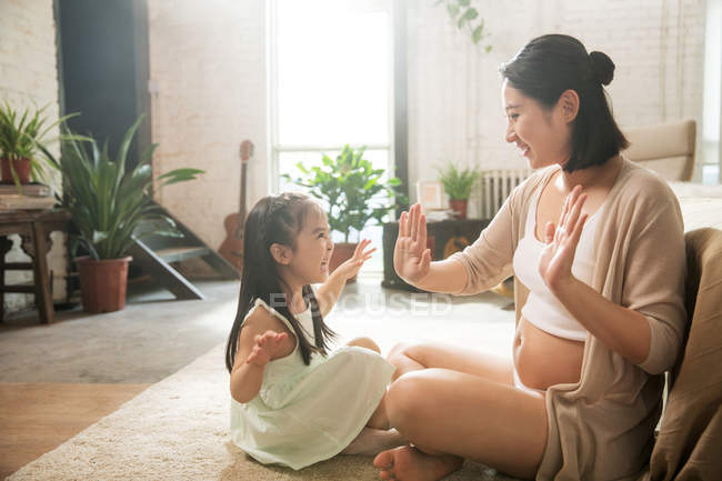 Side view of pregnant mother and happy little girl playing at home — Stock Photo