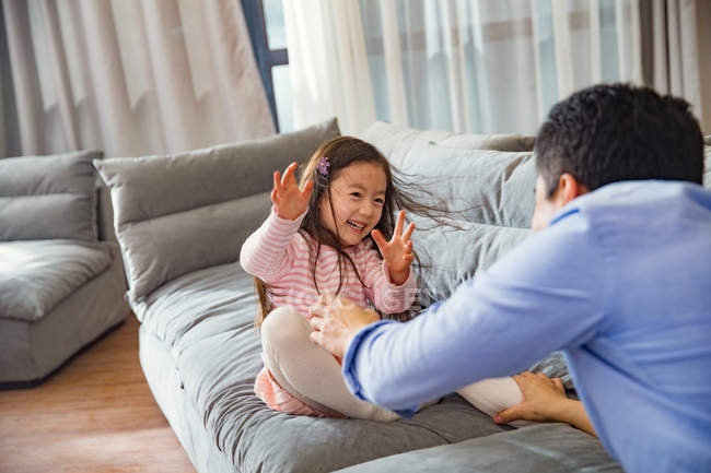 Feliz asiático padre y lindo poco hija jugando y divertirse juntos en sofá - foto de stock