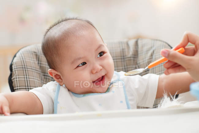 Обрезанный снимок матери, держащей ложку и кормящей очаровательного ребенка — стоковое фото