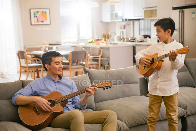 Счастливы, что отец и сын вместе играют на гитарах дома — стоковое фото