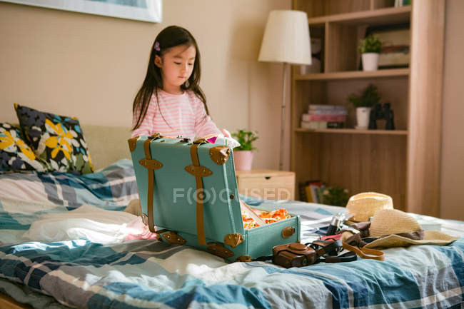 Adorable little asian girl packing suitcase on bed — Stock Photo