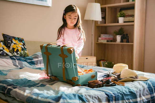 Bonito pouco asiático menina embalagem mala no cama — Fotografia de Stock