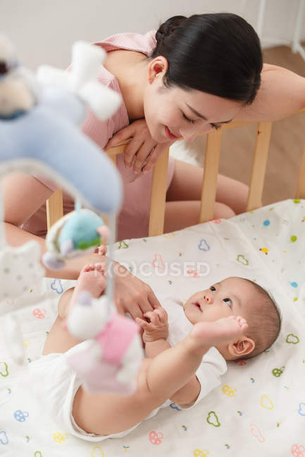 Happy young mother looking at adorable infant baby lying in crib, high angle view — Stock Photo