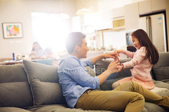 Счастливый отец с очаровательной маленькой дочкой, сидящей и играющей вместе на диване — стоковое фото