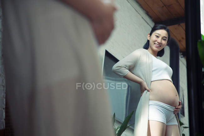 Избирательный фокус счастливой молодой беременной женщины, смотрящей в зеркало — стоковое фото