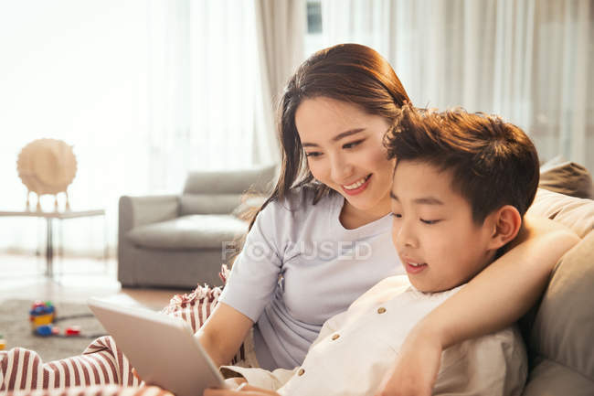 Feliz asiático madre con hijo usando digital tablet juntos en casa - foto de stock